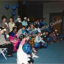 [Three rows of people, many holding blue balloons with white stars]